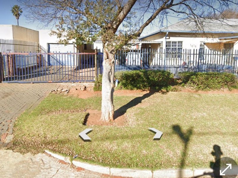 Front view of a residential property featuring a metal security fence, sliding gate, and paved driveway area.