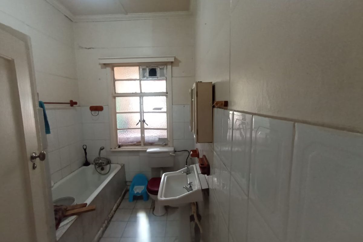 A dated bathroom featuring a bathtub, wall-mounted basin, and toilet with tiled finishes, requiring modernization and cosmetic updates to improve its overall condition.