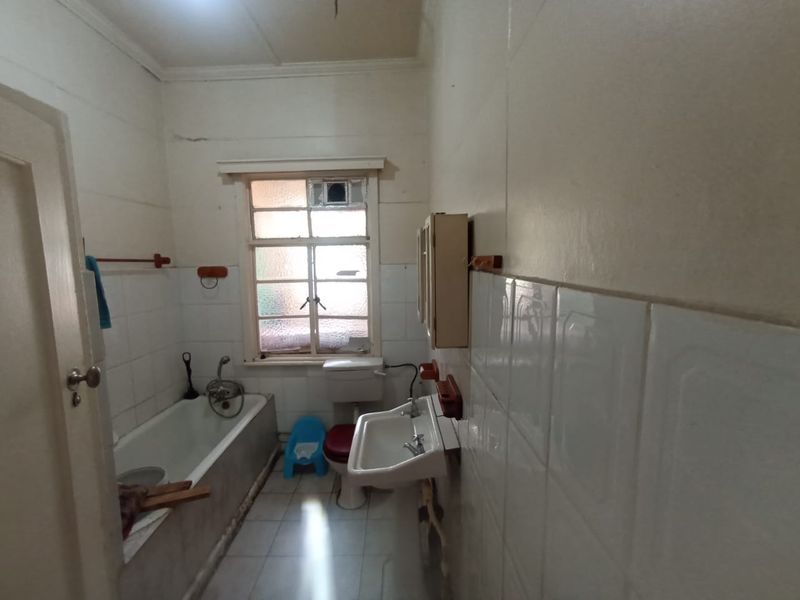 A dated bathroom featuring a bathtub, wall-mounted basin, and toilet with tiled finishes, requiring modernization and cosmetic updates to improve its overall condition.