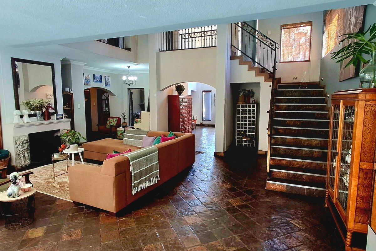 Spacious open-plan living area featuring a fireplace, stone tile flooring, and a prominent staircase leading to a mezzanine landing.