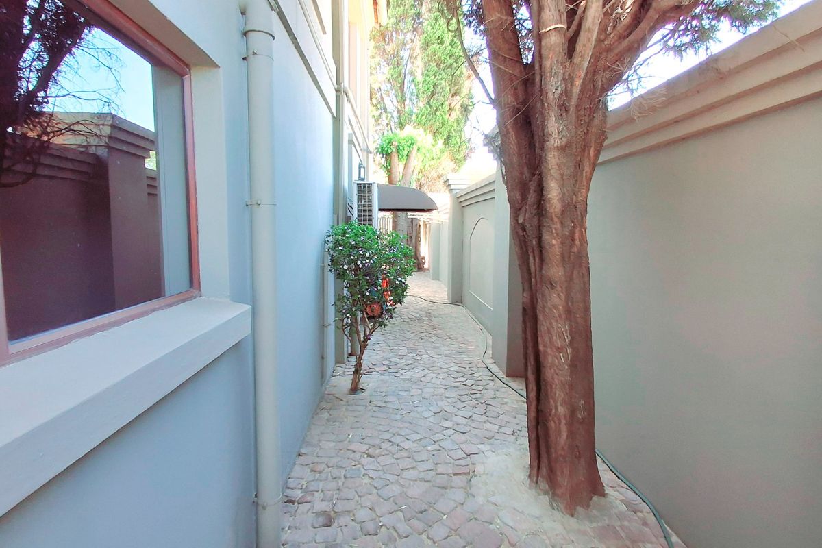 A narrow side passage featuring cobblestone paving, a boundary wall, and a mature tree, providing access along the side of the house.