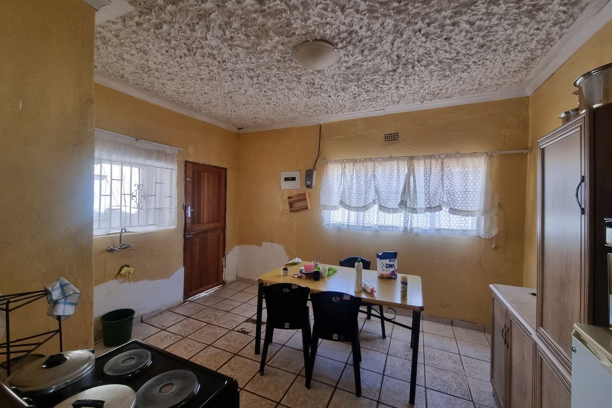 A dated kitchen area featuring tiled floors, textured ceilings, and wall-mounted plumbing, requiring cosmetic updates and wall repairs to modernize the space.