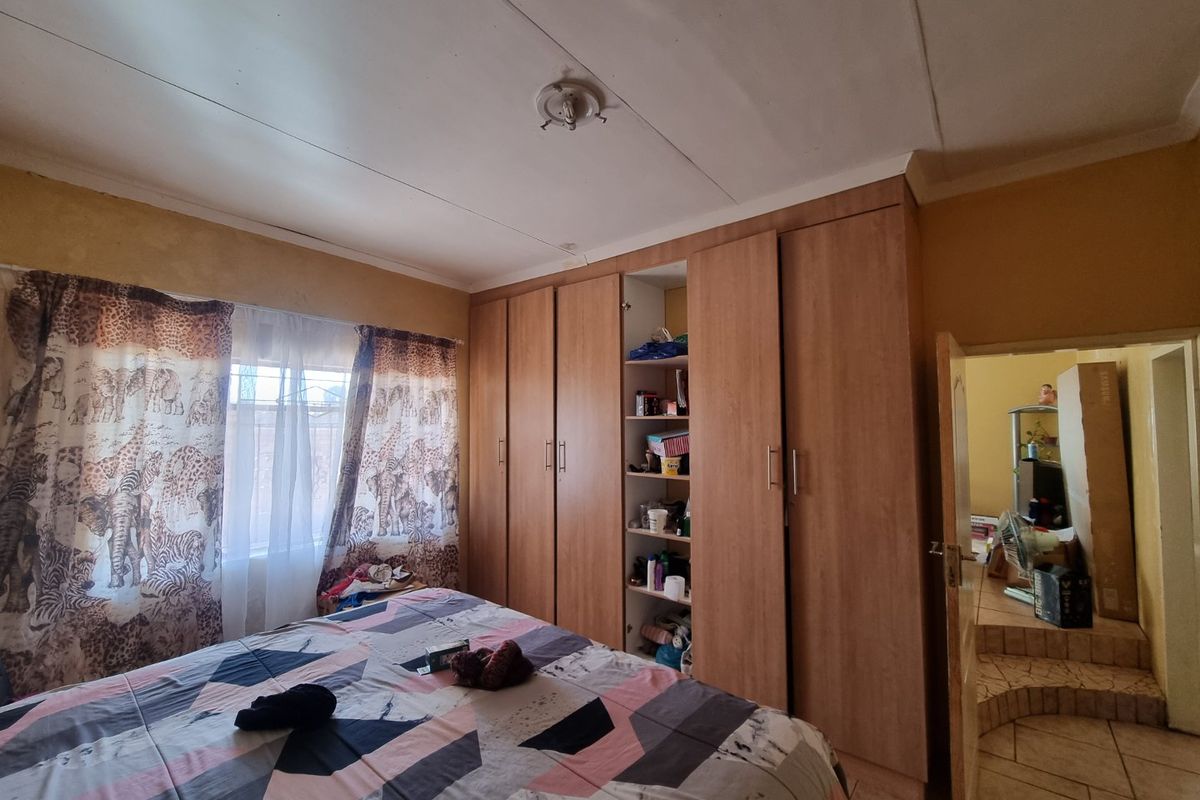 Bedroom featuring a large built-in wooden wardrobe, coving, and a central ceiling light fixture, with visible signs of wear on the ceiling and walls.