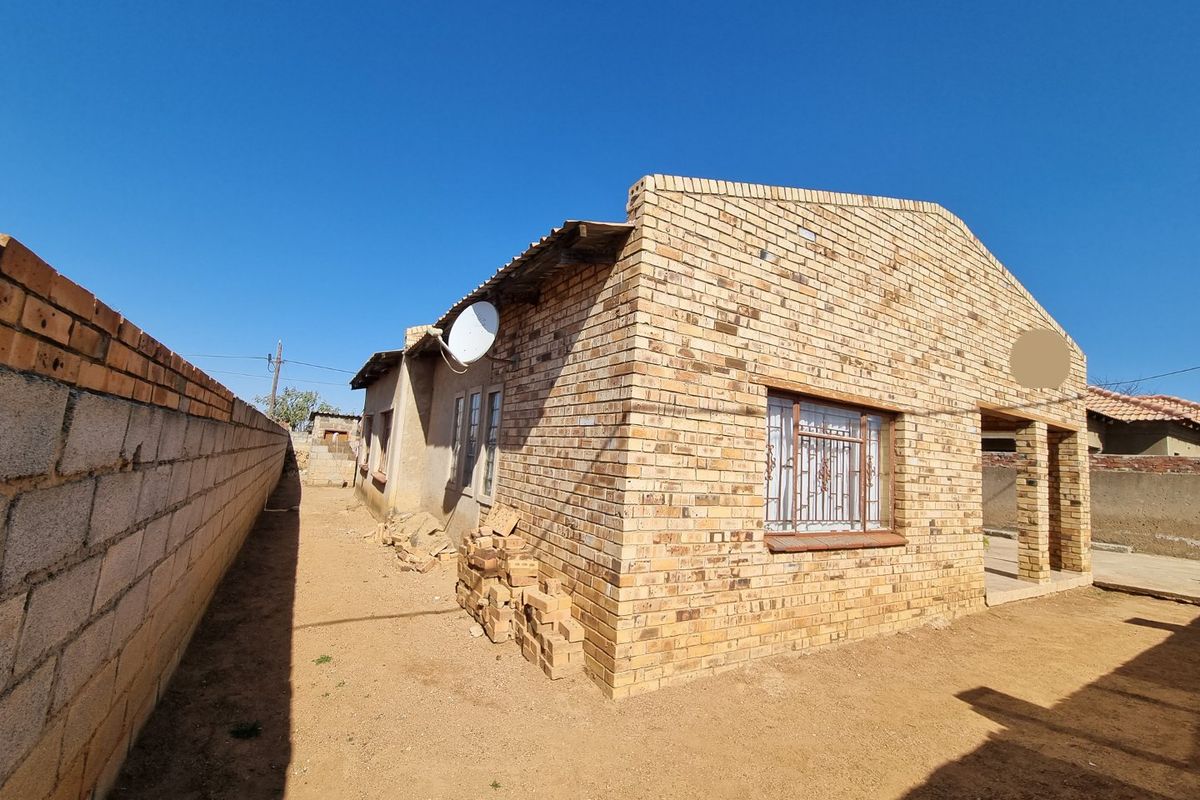 Rear view of a face brick house featuring security bars on windows and a surrounding boundary wall.