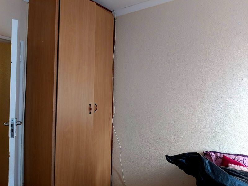 A bedroom featuring a built-in wooden wardrobe with visible electrical wiring running along the wall corner.