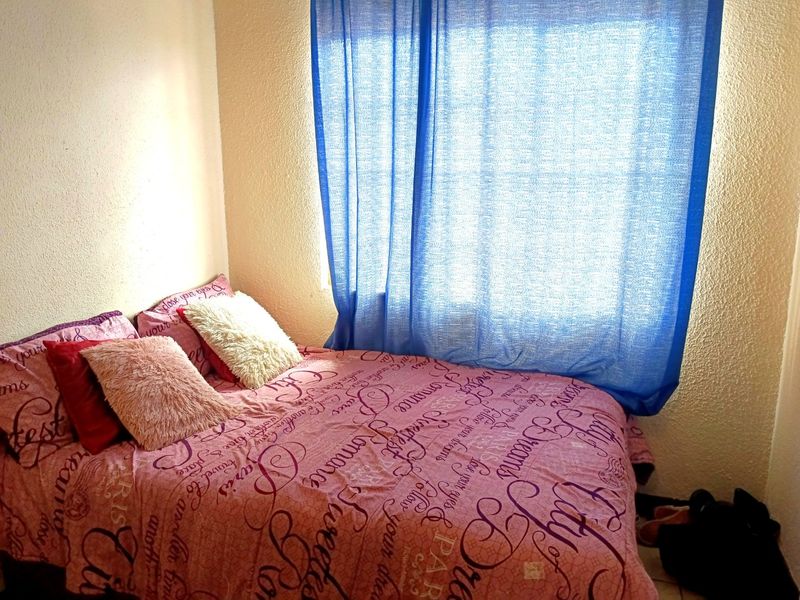 A compact bedroom featuring a window with blue curtains and textured wall finishes.