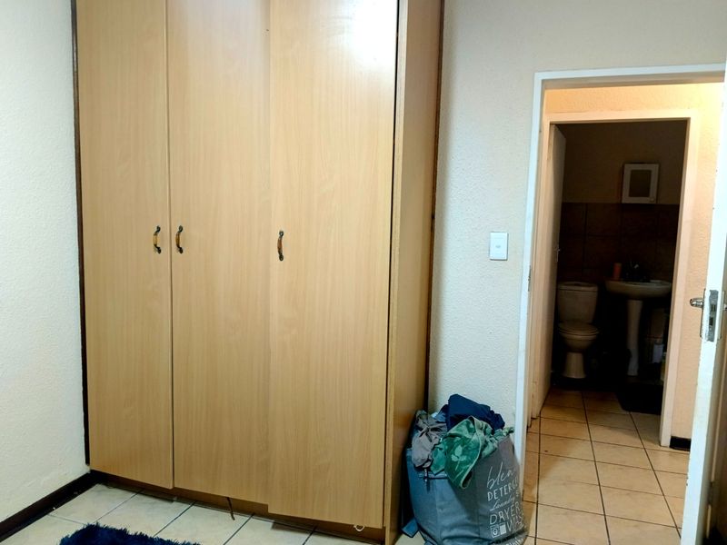 A bedroom featuring a large built-in wooden wardrobe and tiled flooring, with an adjacent view into a bathroom.