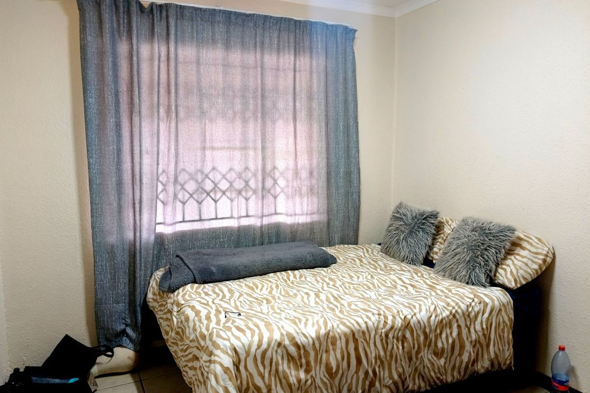 A standard bedroom featuring tiled flooring, a window with a security gate, and neutral wall finishes.