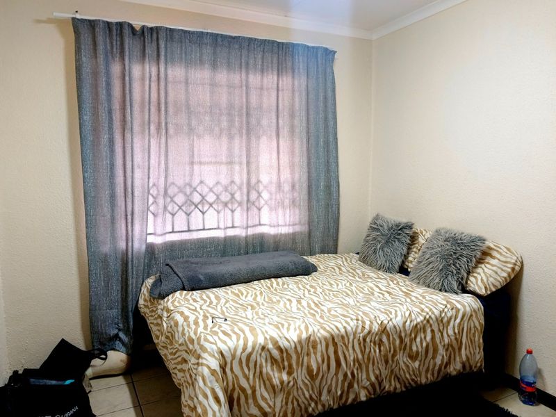 A standard bedroom featuring tiled flooring, a window with a security gate, and neutral wall finishes.