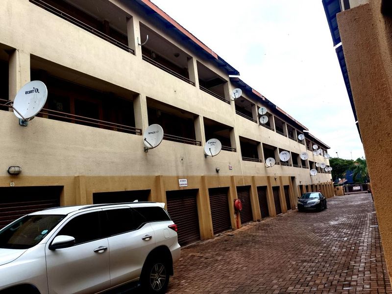 Exterior view of an apartment complex featuring a paved driveway, multiple garage units, and balconies with satellite dish installations.