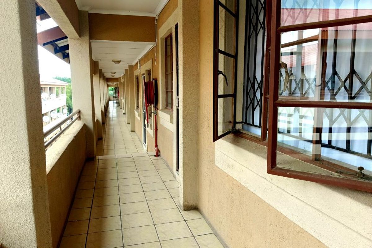 An exterior covered apartment walkway featuring tiled flooring, security bars on windows, and a wall-mounted fire hose reel.