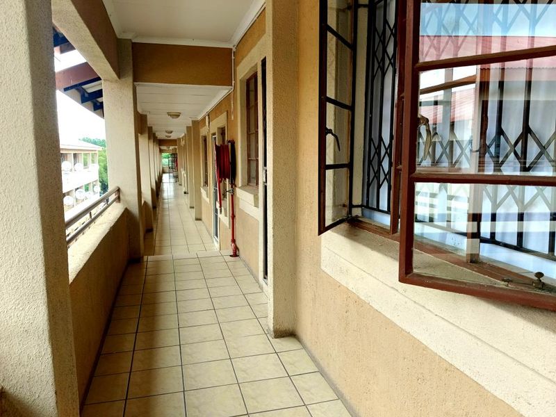 An exterior covered apartment walkway featuring tiled flooring, security bars on windows, and a wall-mounted fire hose reel.