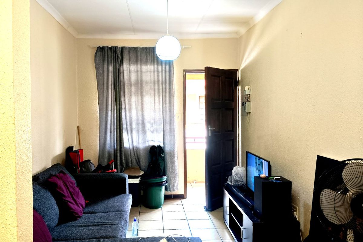 A compact living room featuring tiled flooring and direct access to an outdoor area, providing a functional space with potential for cosmetic updates.