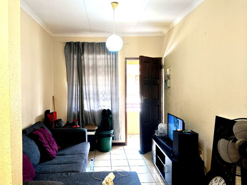 A compact living room featuring tiled flooring and direct access to an outdoor area, providing a functional space with potential for cosmetic updates.