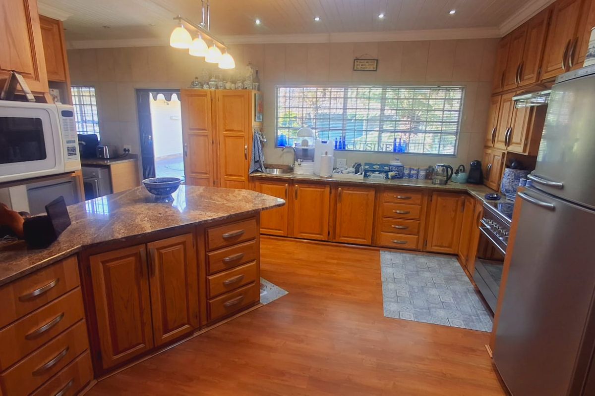 Spacious kitchen featuring warm wooden cabinetry, granite countertops, a central island, and integrated appliances, offering a functional layout with ample storage space.