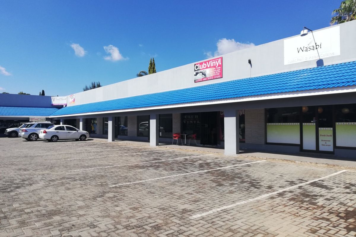 Front exterior view of a commercial strip mall featuring multiple storefronts, a covered walkway, and a paved parking area.