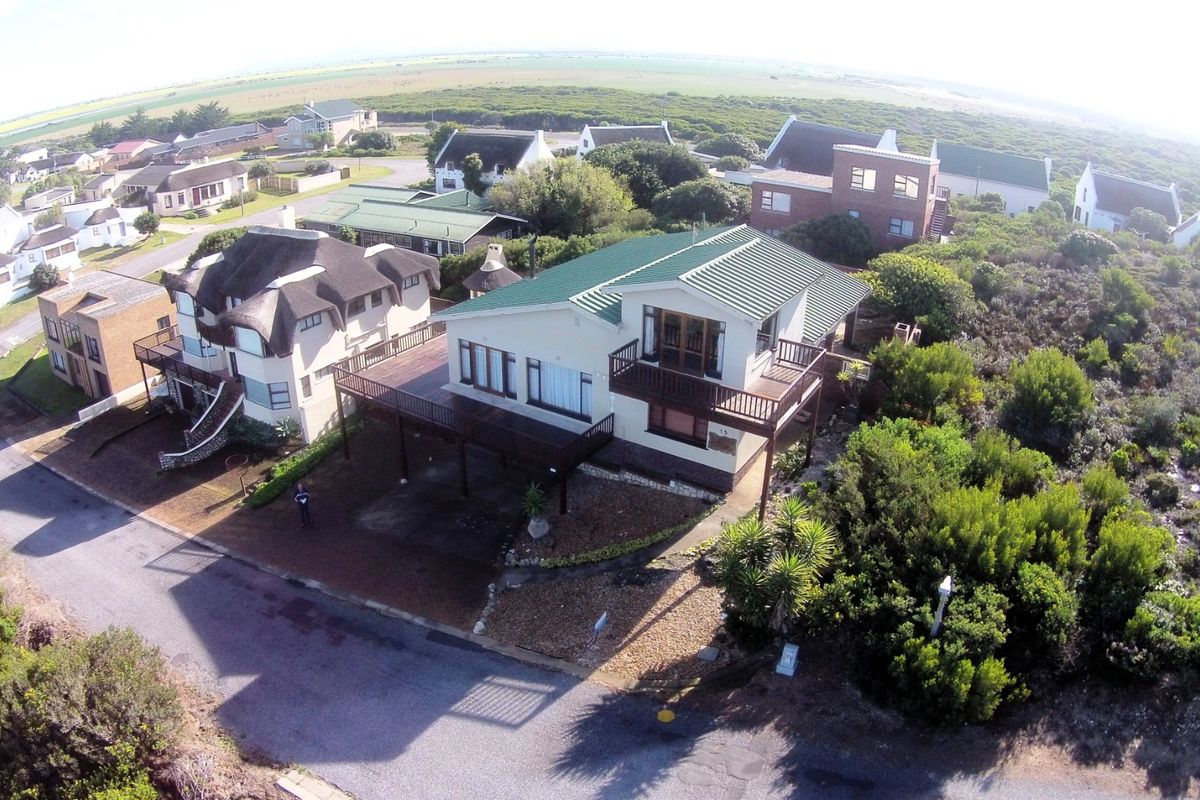 Aerial view of a coastal residential property featuring a metal roof, elevated timber decking, and surrounding landscaped garden area.