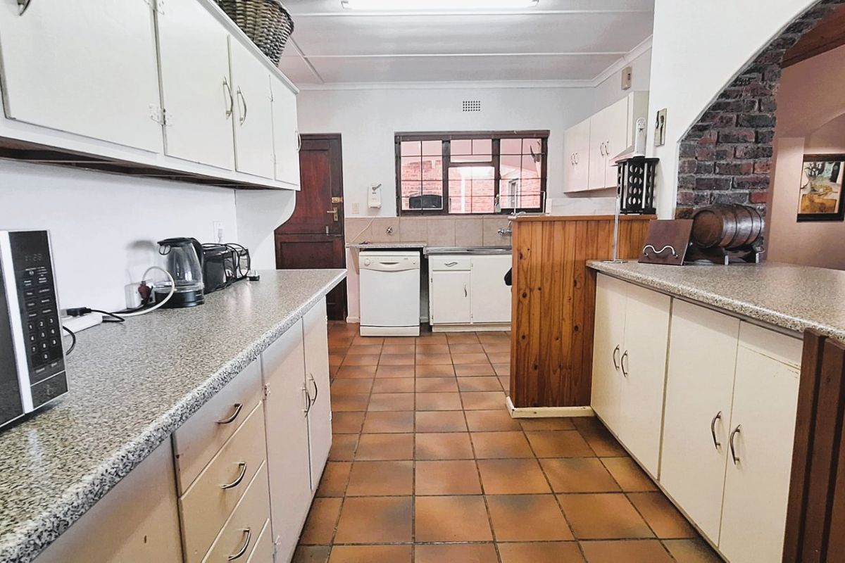 A functional kitchen featuring laminate cabinetry, granite-look countertops, and an exposed brick feature wall, offering a classic layout with potential for modernization.