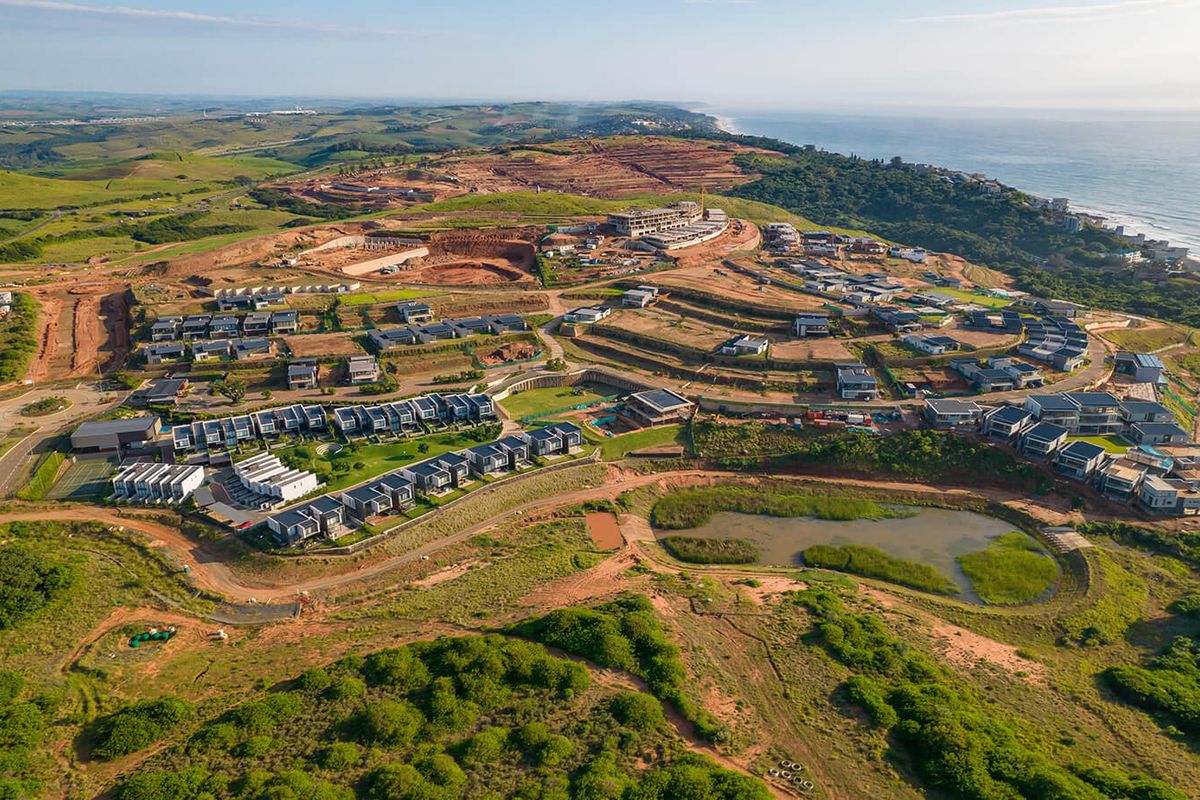 Aerial view of a modern residential estate development situated on a coastal hillside, featuring established housing clusters and ongoing construction phases.