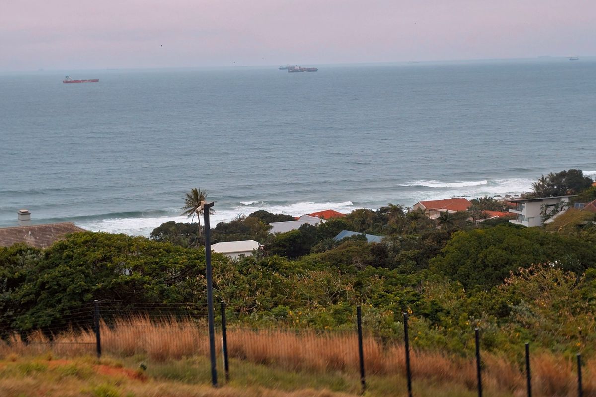 An elevated coastal view overlooking the ocean, surrounding residential properties, and lush greenery, captured from the vacant land site.