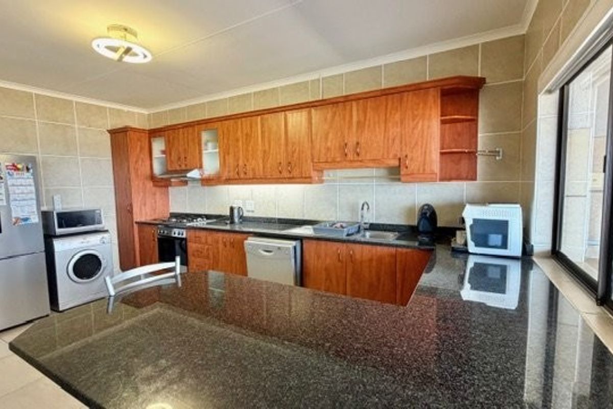 A functional kitchen featuring wooden cabinetry, granite countertops, a built-in oven, hob, and tiled finishes throughout.