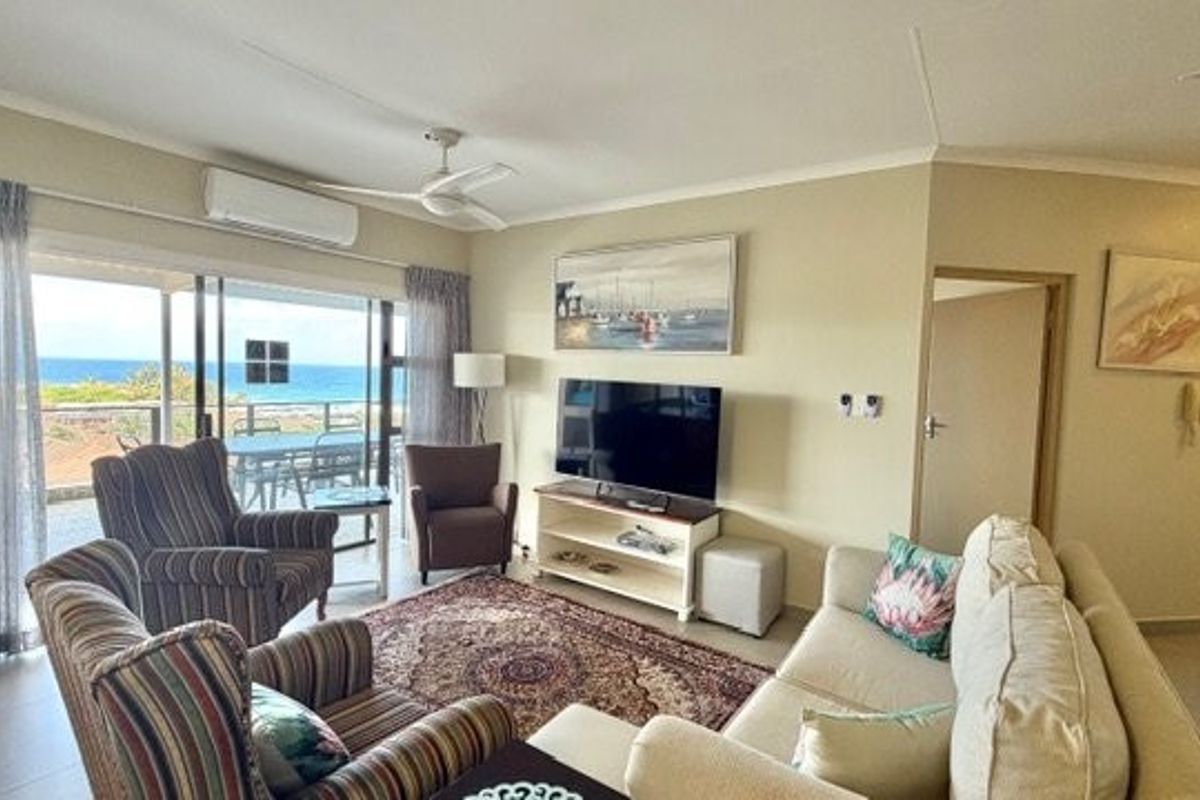 A comfortable living room featuring tiled floors, a split-system air conditioner, and large sliding glass doors that open to a scenic ocean view.