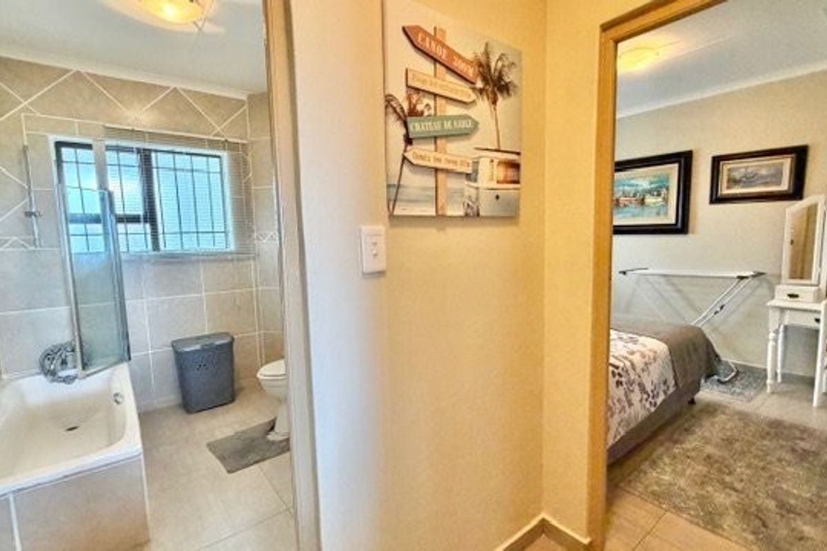 A functional bathroom featuring tiled walls and flooring, a bathtub with a shower screen, and a toilet, adjacent to a bedroom area.