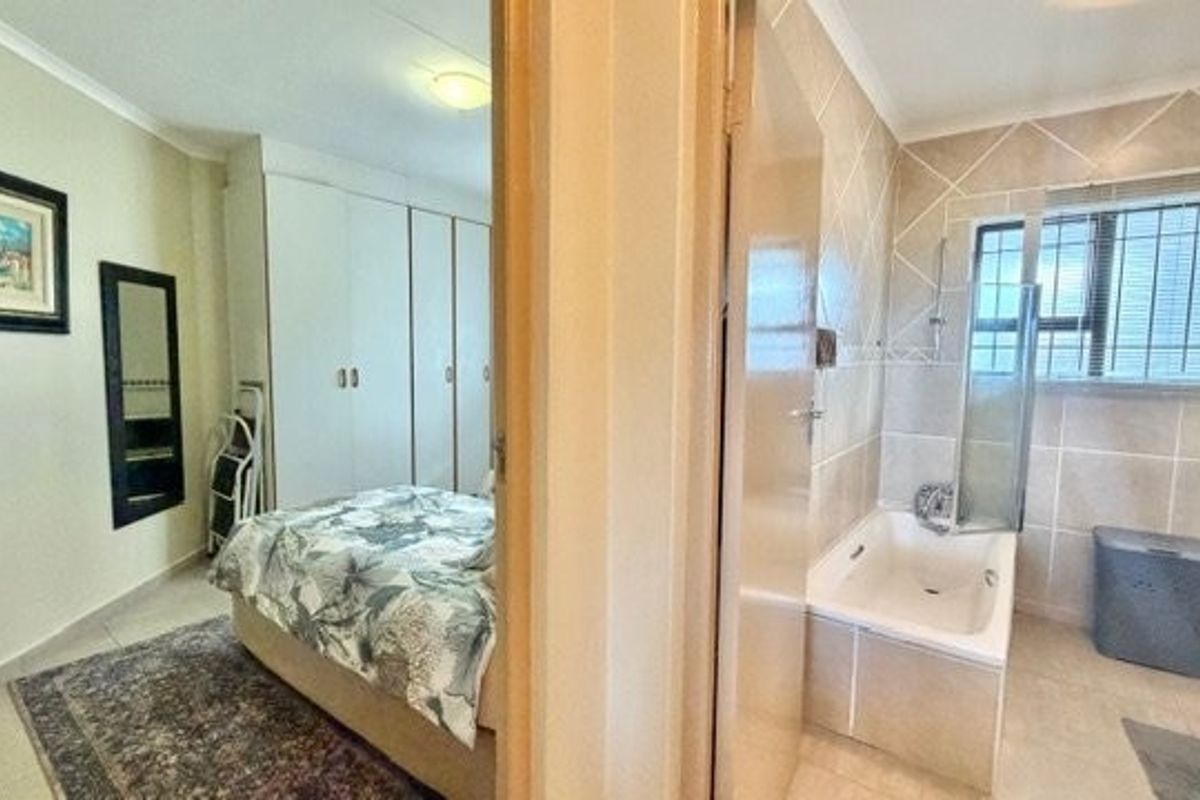 A bedroom featuring built-in cupboards and an adjacent bathroom with a tiled bathtub and shower screen.