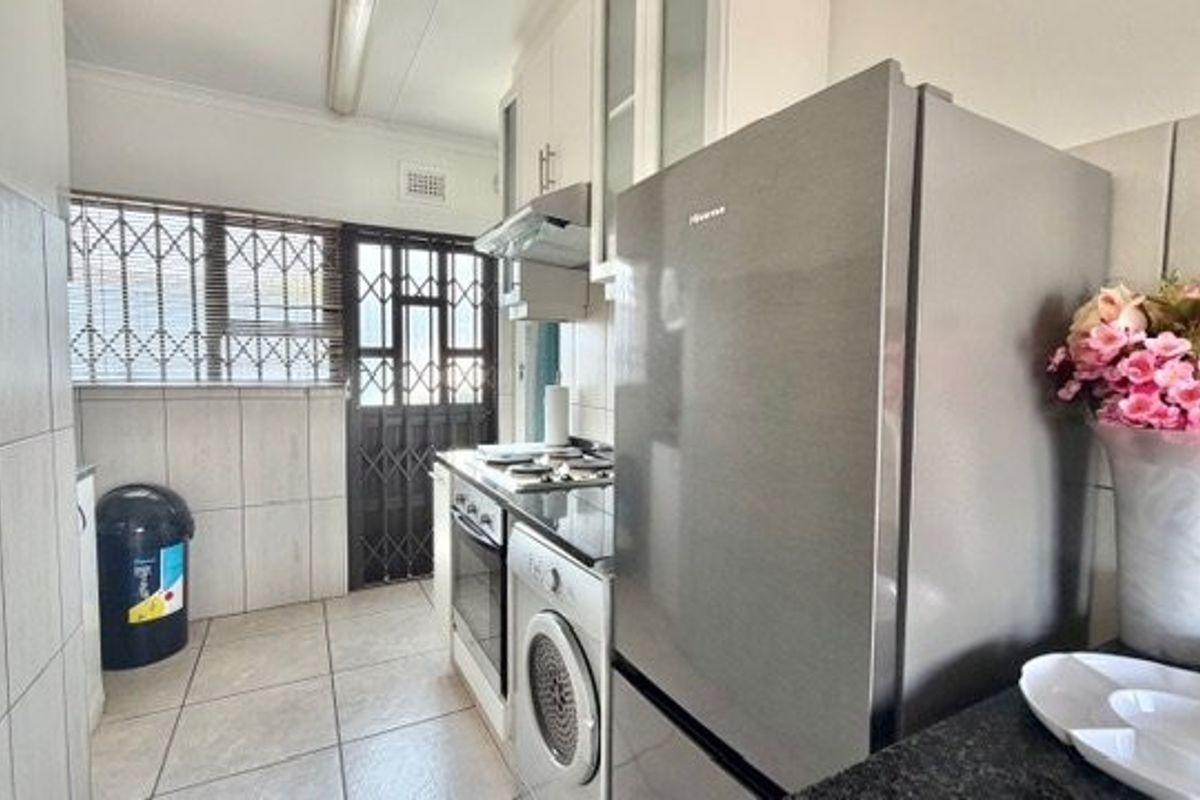 A functional kitchen featuring built-in cabinetry, integrated appliances, tiled flooring, and secure access points with security gates and bars.