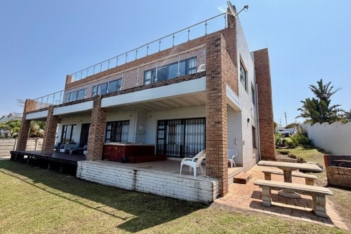 Rear view of a multi-story brick house featuring a spacious covered patio, a large upper-level balcony with glass balustrades, and a paved outdoor seating area.