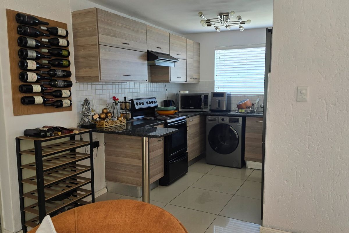 Compact kitchen featuring modern laminate cabinetry, granite countertops, tiled backsplash, and integrated laundry facilities, offering a functional and efficient workspace.