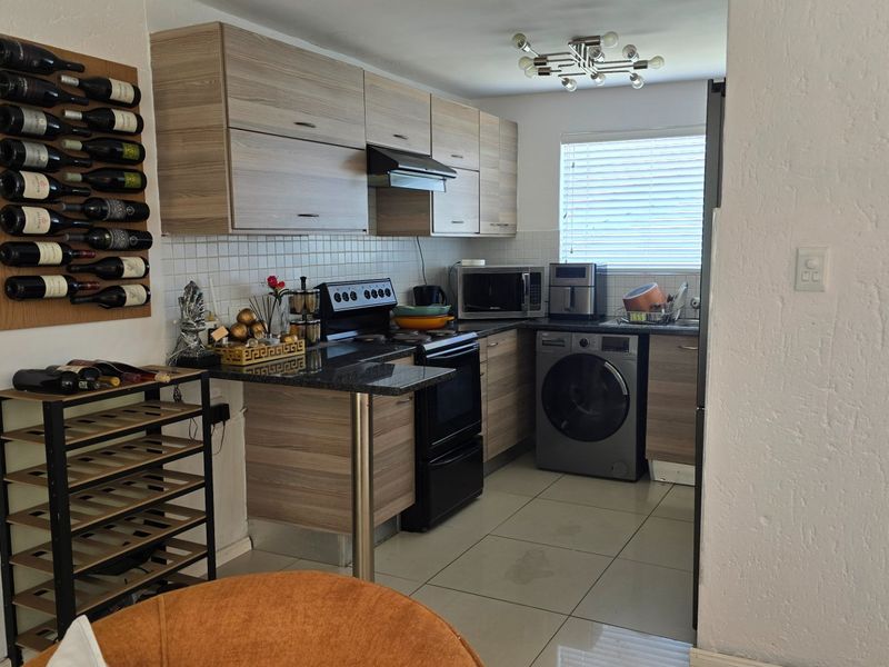 Compact kitchen featuring modern laminate cabinetry, granite countertops, tiled backsplash, and integrated laundry facilities, offering a functional and efficient workspace.