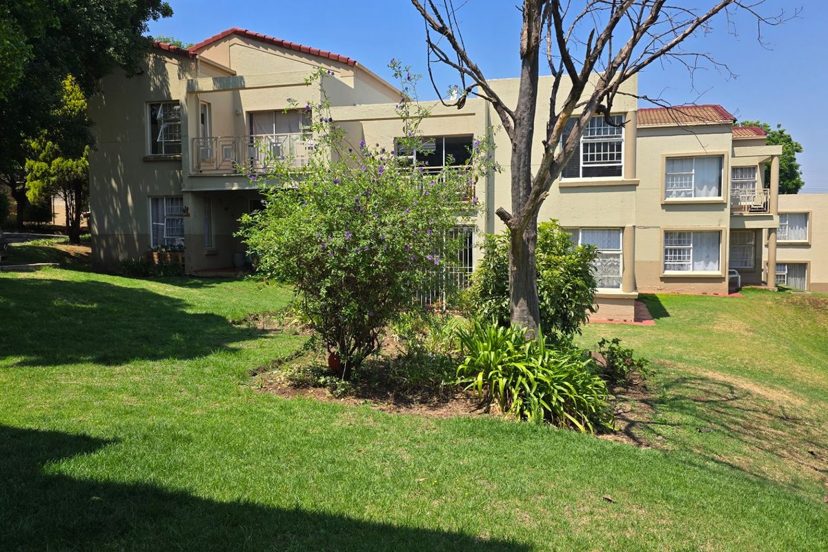 Rear view of the apartment complex featuring a shared garden, balconies, and established landscaping.