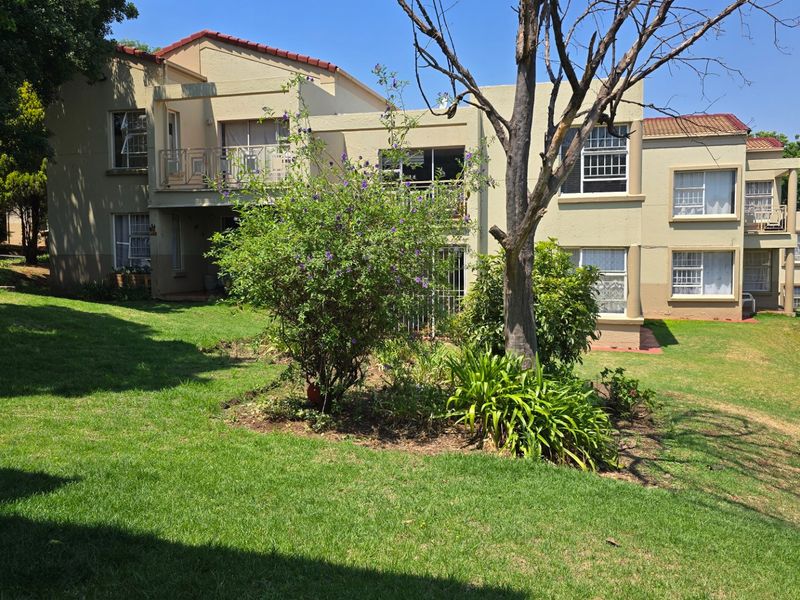 Rear view of the apartment complex featuring a shared garden, balconies, and established landscaping.