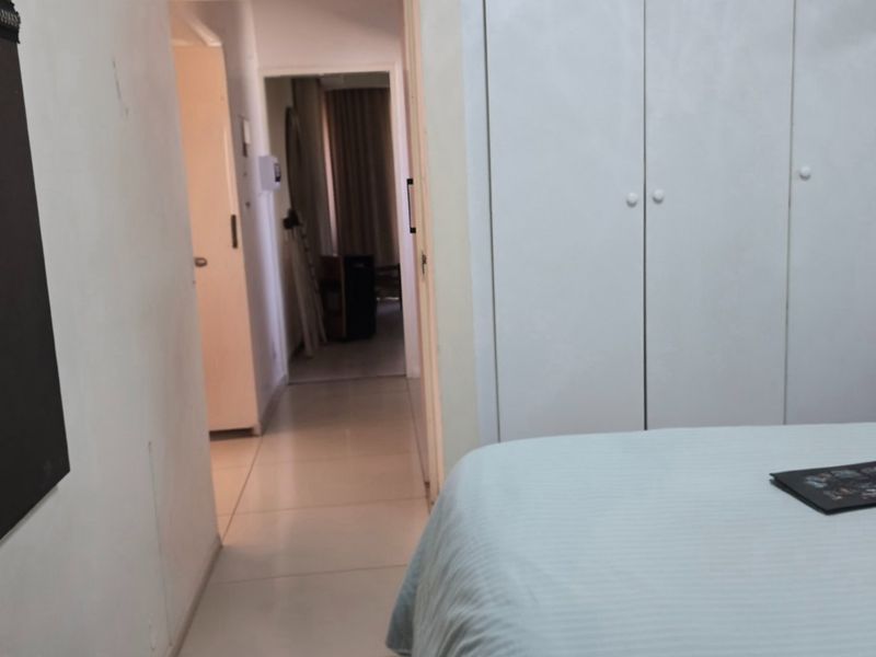 A bedroom featuring built-in cupboards and tiled flooring, with a view leading into an adjacent hallway.