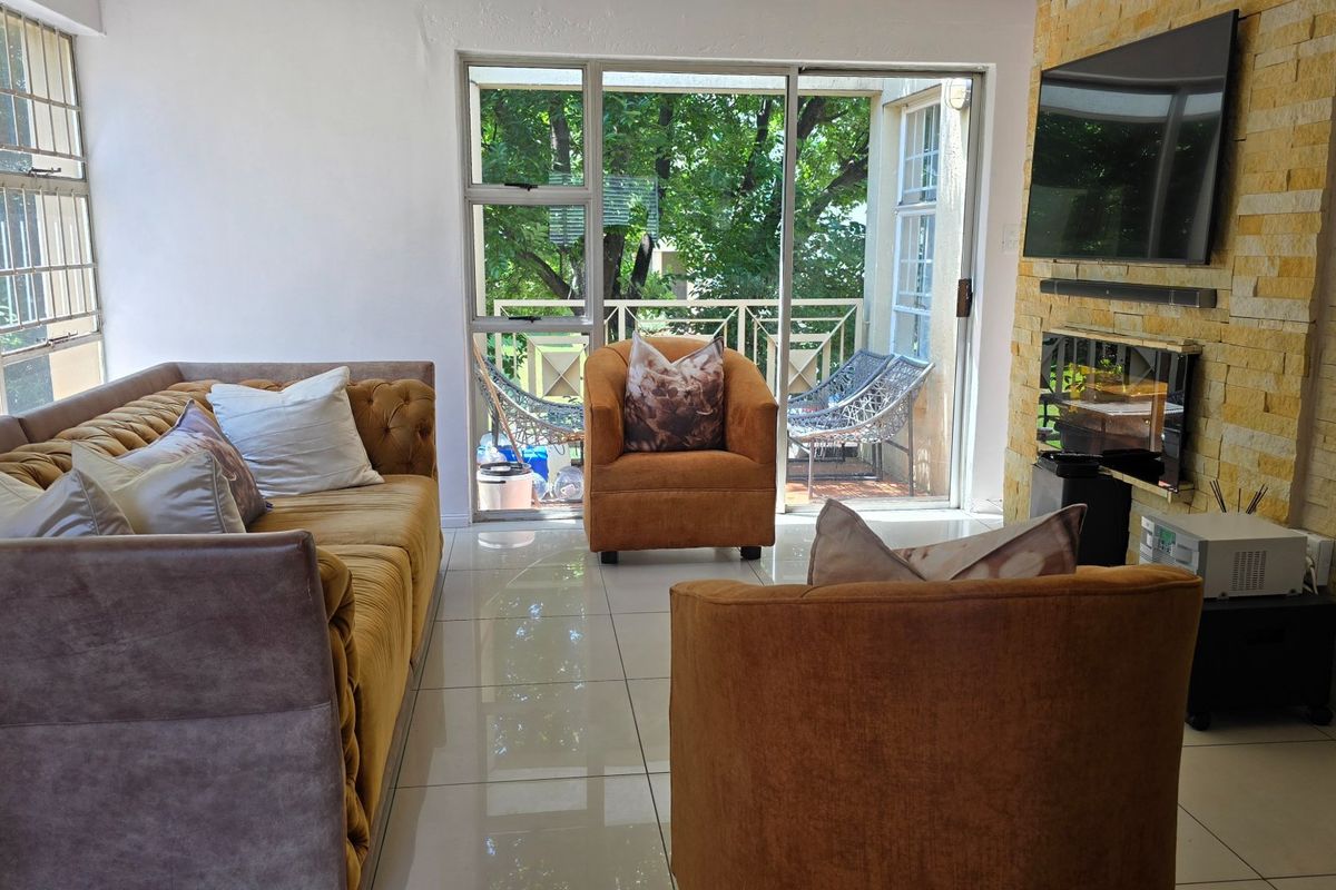 A bright living room featuring a stone-clad feature wall, polished tile flooring, and large sliding glass doors providing access to an outdoor balcony area.