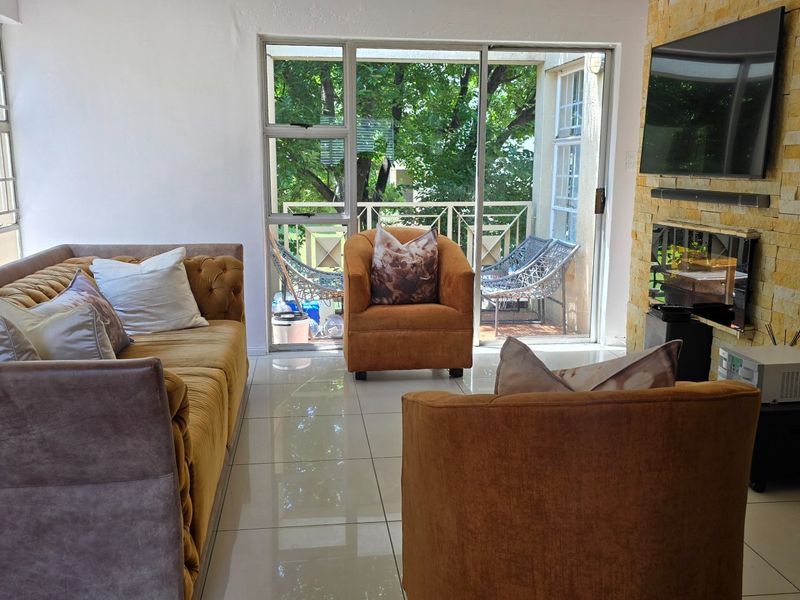 A bright living room featuring a stone-clad feature wall, polished tile flooring, and large sliding glass doors providing access to an outdoor balcony area.
