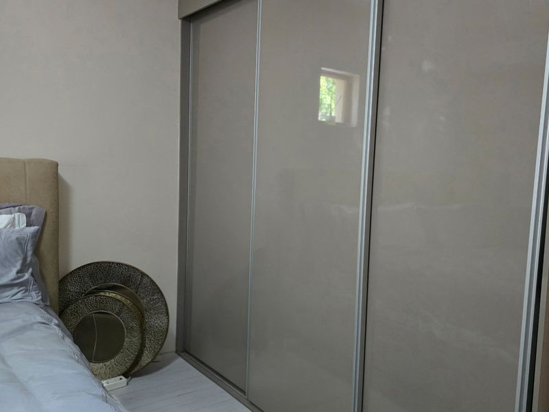 A bedroom featuring modern, high-gloss sliding door built-in wardrobes and light-toned laminate flooring.