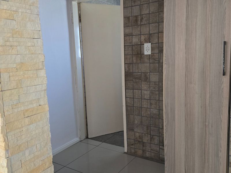 A hallway featuring a stone-clad accent wall, textured wall tiling, and a built-in cupboard with neutral floor tiles.