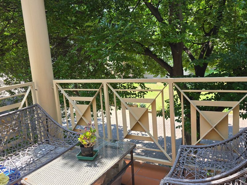 A private balcony featuring a decorative metal balustrade, tiled flooring, and a support column, overlooking lush greenery.