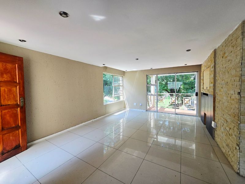 Spacious, empty living area featuring large format floor tiles, a stone-clad feature wall, recessed lighting, and sliding door access to an outdoor balcony.