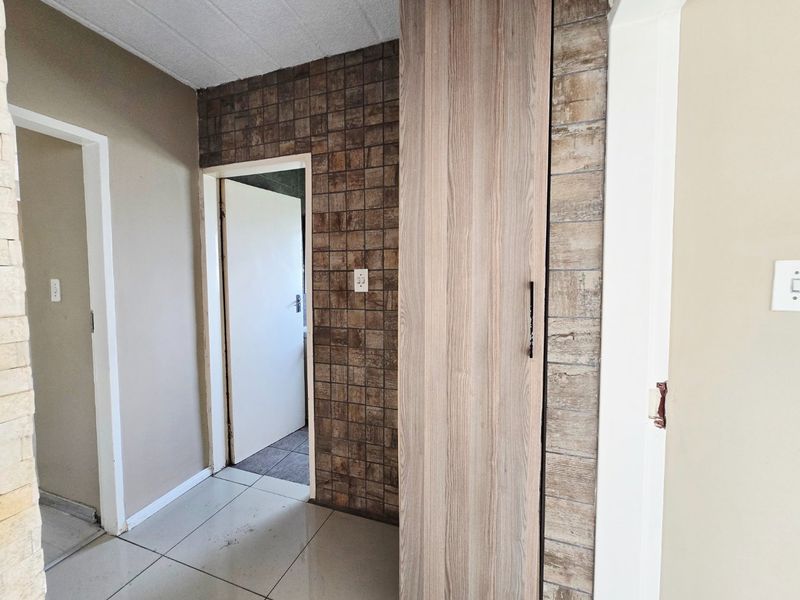 A functional hallway featuring built-in storage cabinetry, tiled flooring, and decorative wall cladding, providing access to adjacent rooms within the apartment.