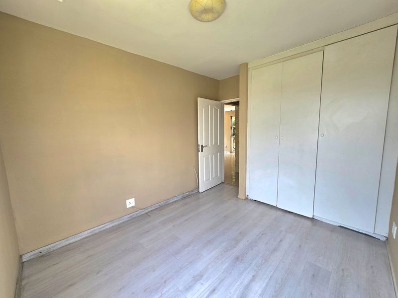 An empty bedroom featuring light-toned laminate flooring and built-in white cupboards, offering a neutral canvas for personalization.