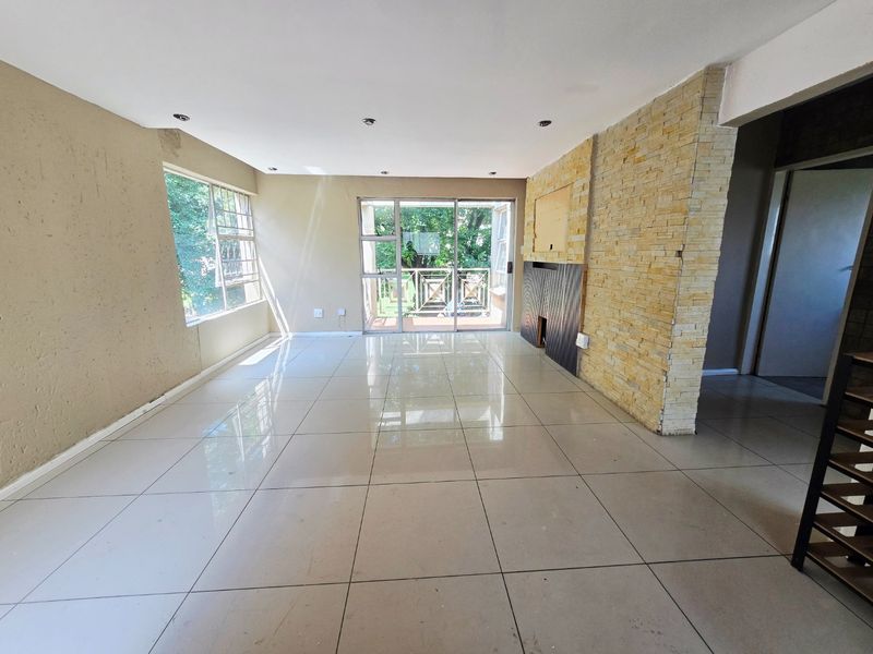 Spacious open-plan living area featuring large format floor tiles, a decorative stone feature wall, and sliding glass doors leading to an outdoor balcony.
