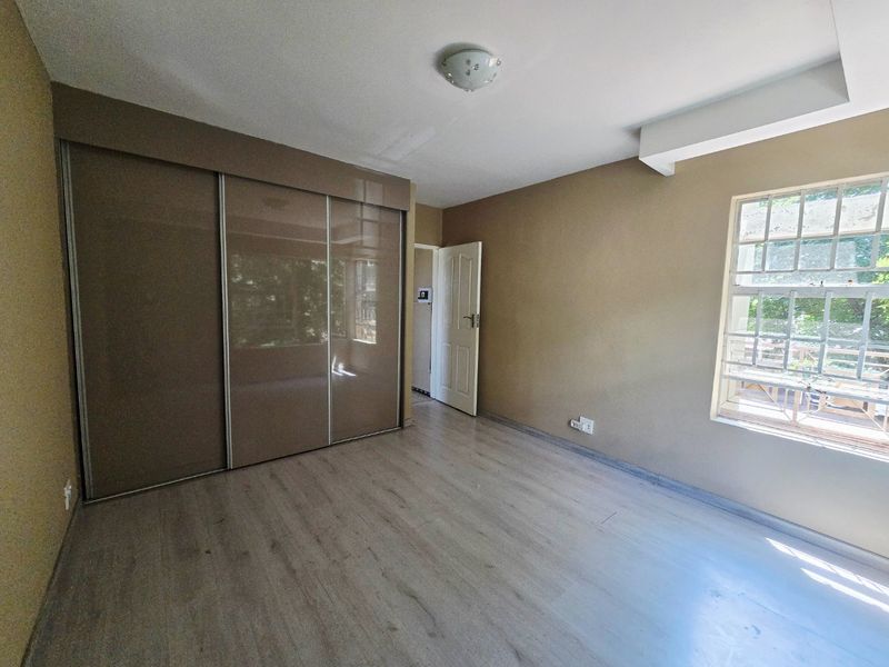 A spacious, empty bedroom featuring modern laminate flooring, a large built-in sliding door wardrobe, and natural light through a window with security bars.