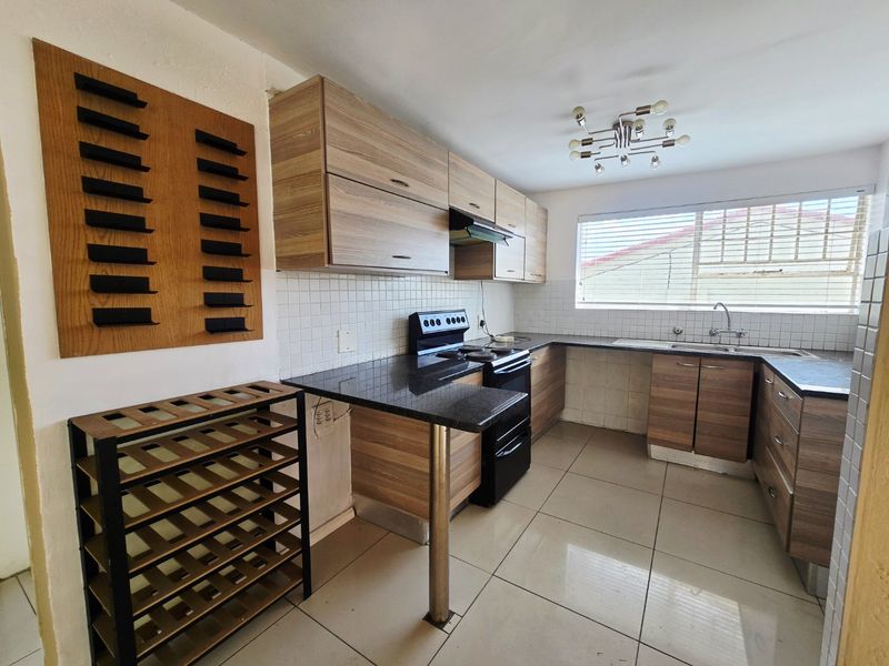 A functional kitchen featuring wood-look cabinetry, granite countertops, a tiled backsplash, and a freestanding stove, offering a practical layout for daily cooking.
