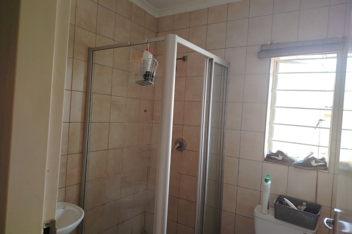 A functional bathroom featuring a shower enclosure, pedestal basin, and toilet with tiled walls and security bars on the window.
