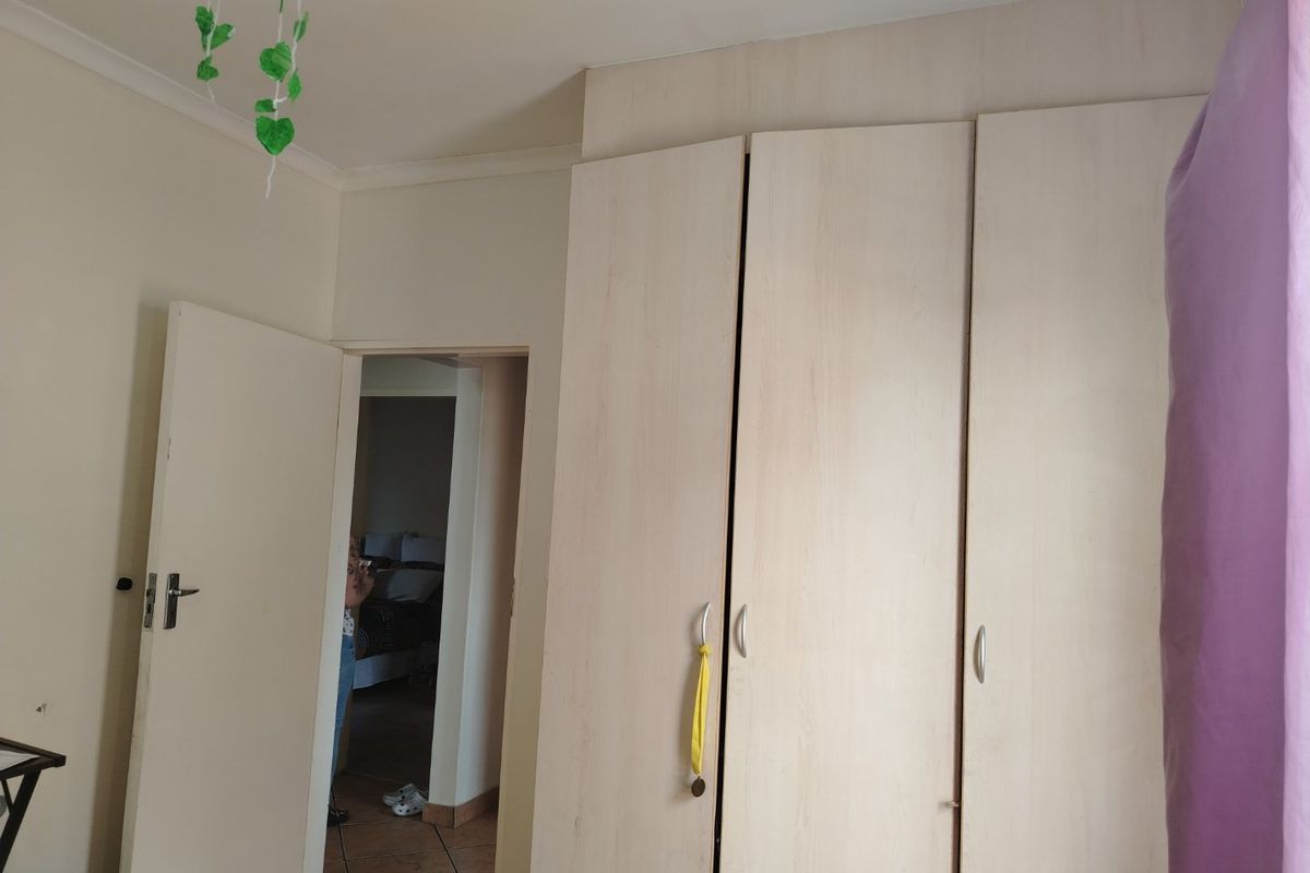 A bedroom featuring light wood-finish built-in cupboards and tiled flooring, with a doorway leading to an adjacent room.