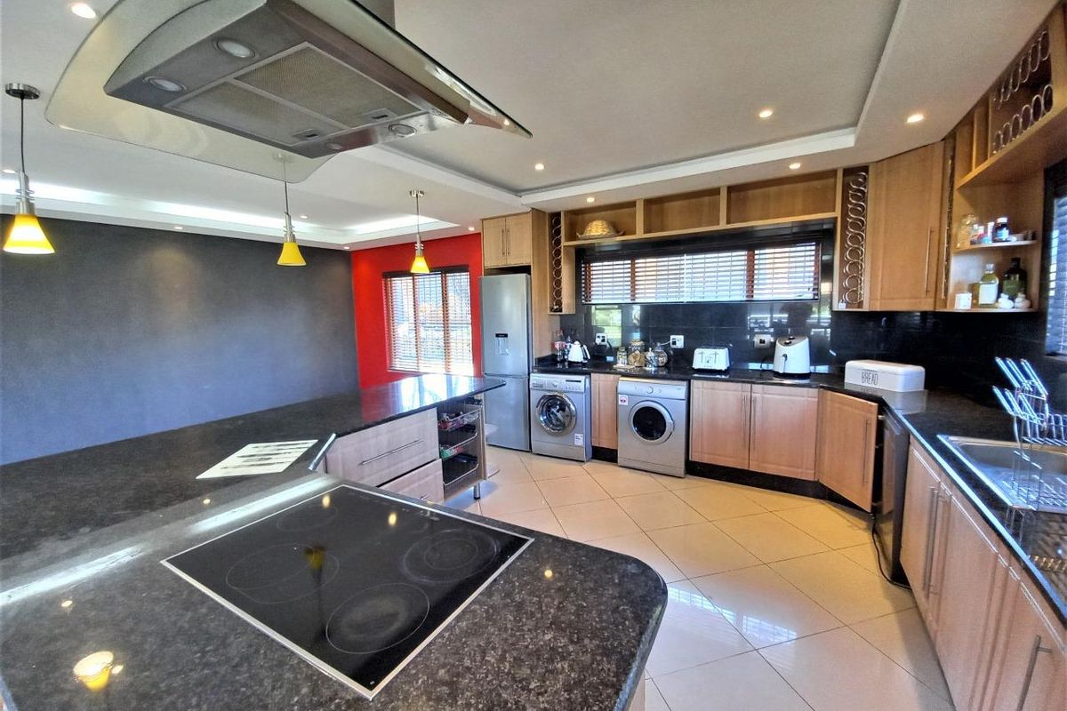 Modern kitchen featuring granite countertops, built-in cabinetry, integrated appliances, and a central island with an electric hob and extractor fan.