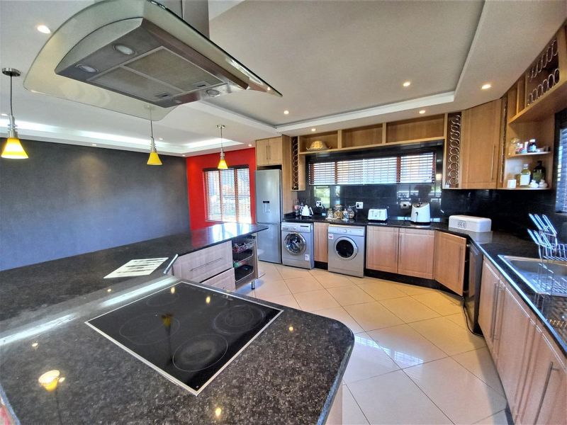 Modern kitchen featuring granite countertops, built-in cabinetry, integrated appliances, and a central island with an electric hob and extractor fan.
